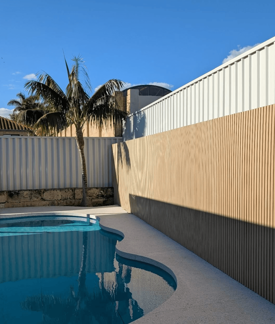 White painted Colorbond fence and natural timber slat feature wall beside a swimming pool in Hallam