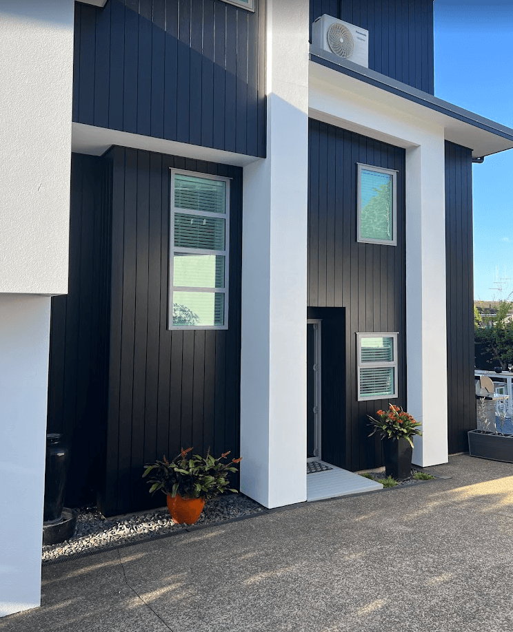 Contemporary two-story residential exterior painting in Berwick featuring dark cladding and white rendered pillars.