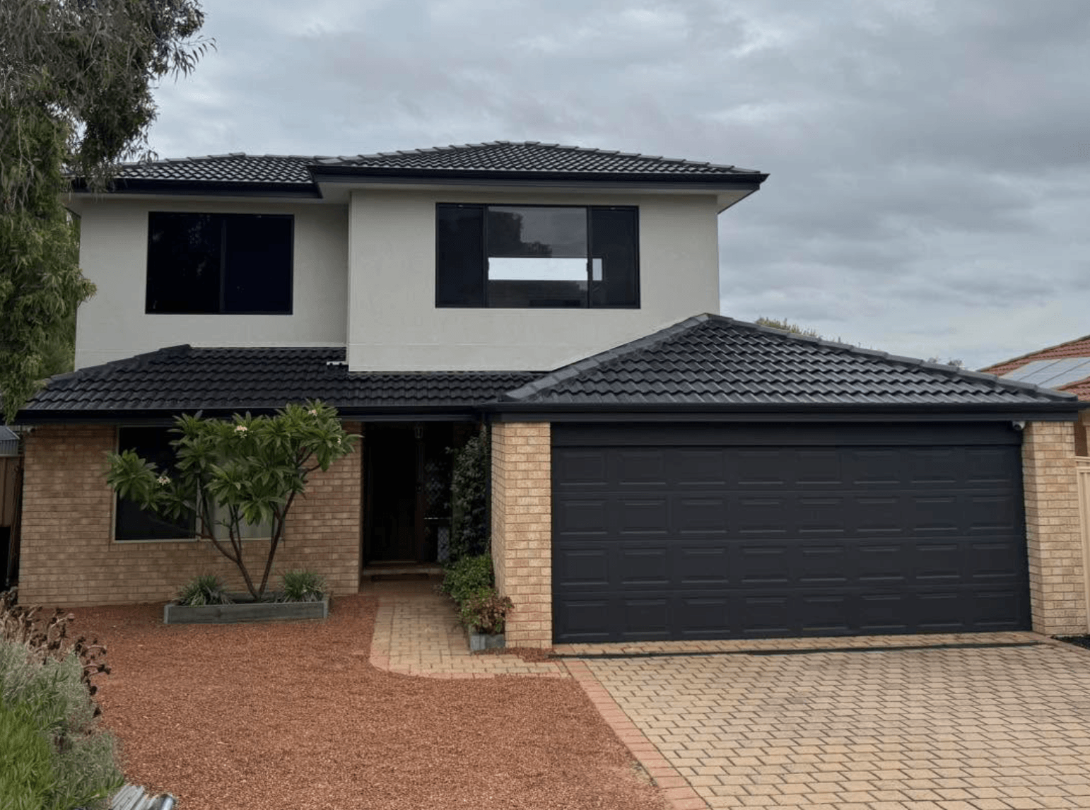 Two-storey home with a freshly coated charcoal concrete tile roof and matching garage door, painted by Northern Star Painting