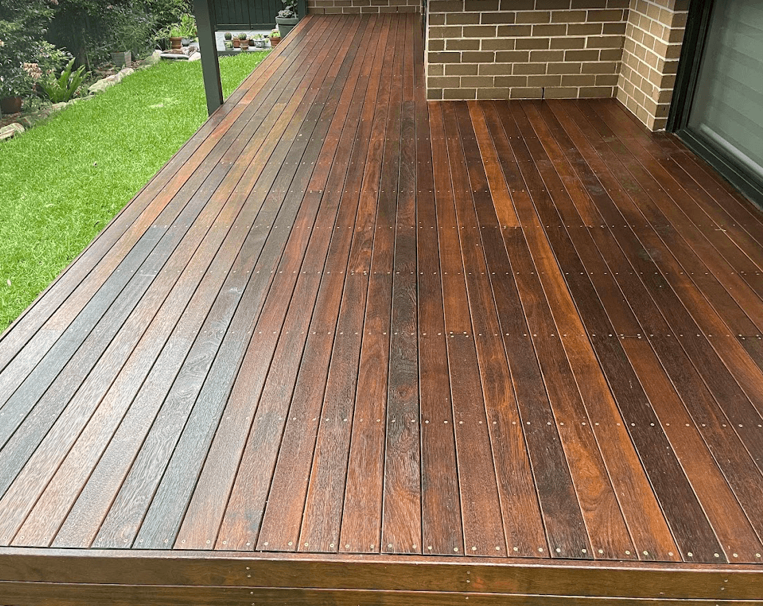 Restored hardwood deck with a rich stained finish beside a brick home and lawn in Berwick