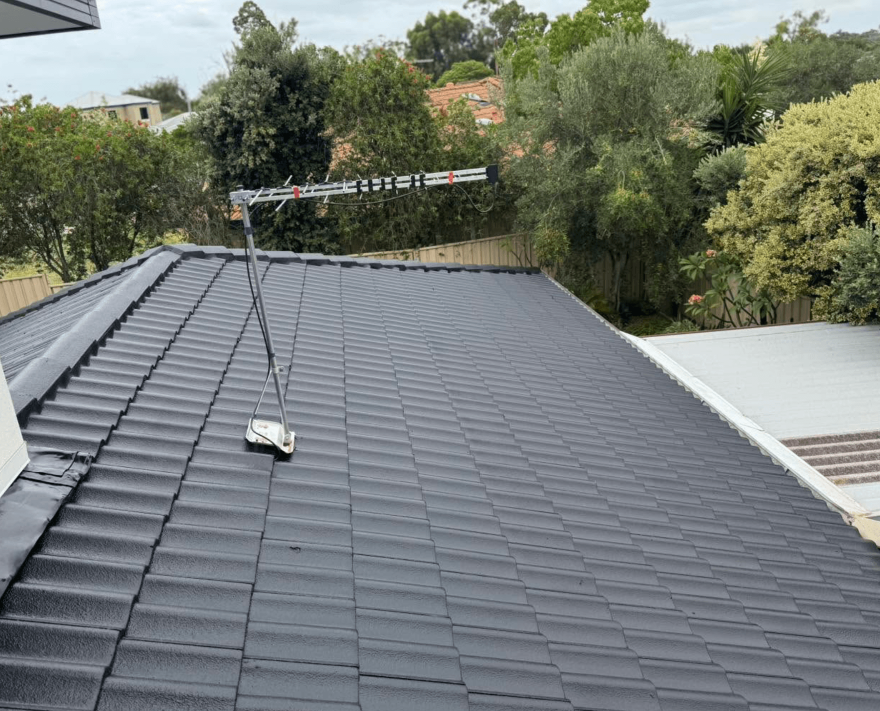 Freshly coated charcoal concrete tile roof surrounded by established trees, painted by Northern Star Painting