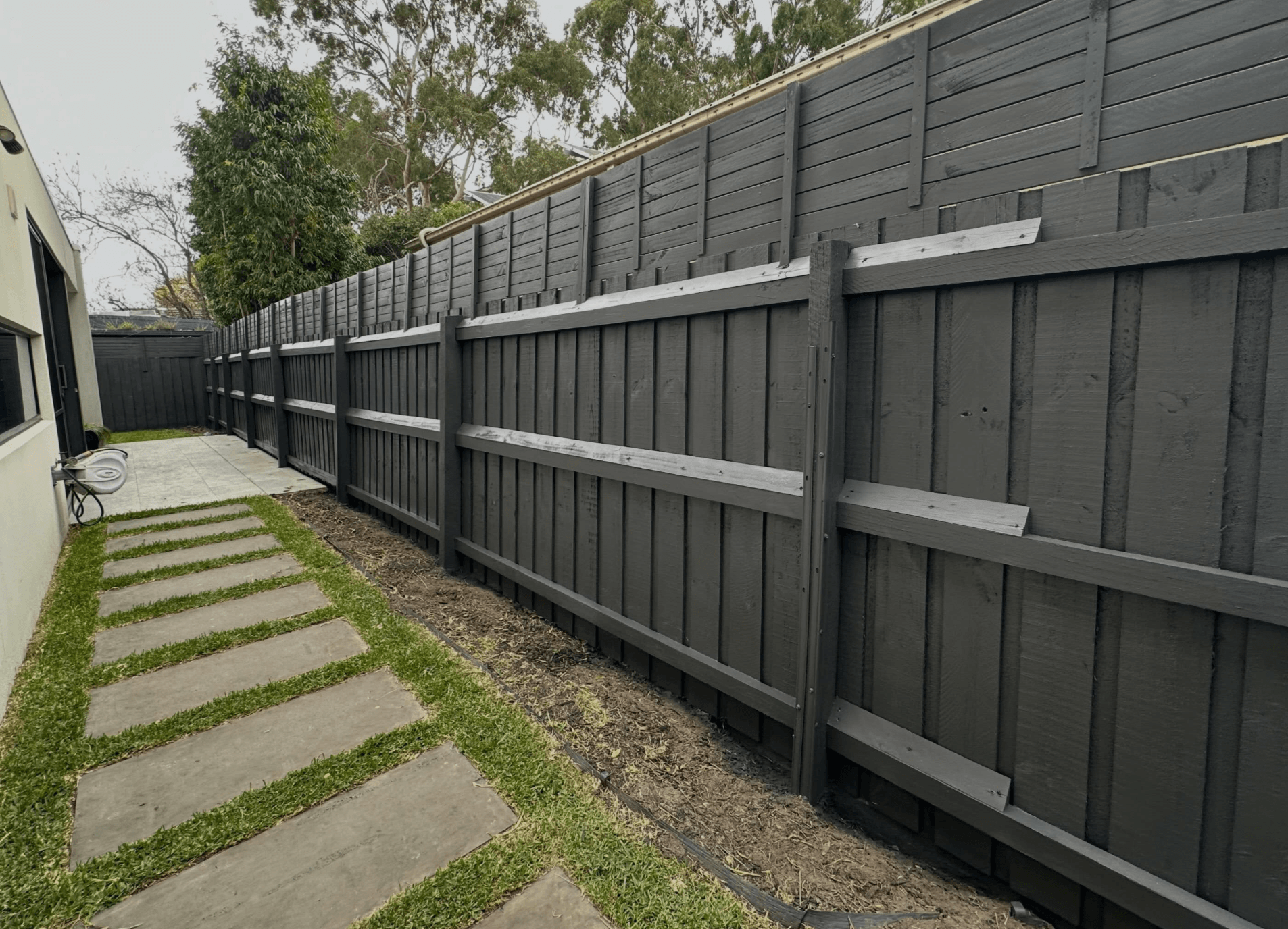 Long grey painted timber paling boundary fence along a paved side path in Narre Warren North, painted by Northern Star Painting