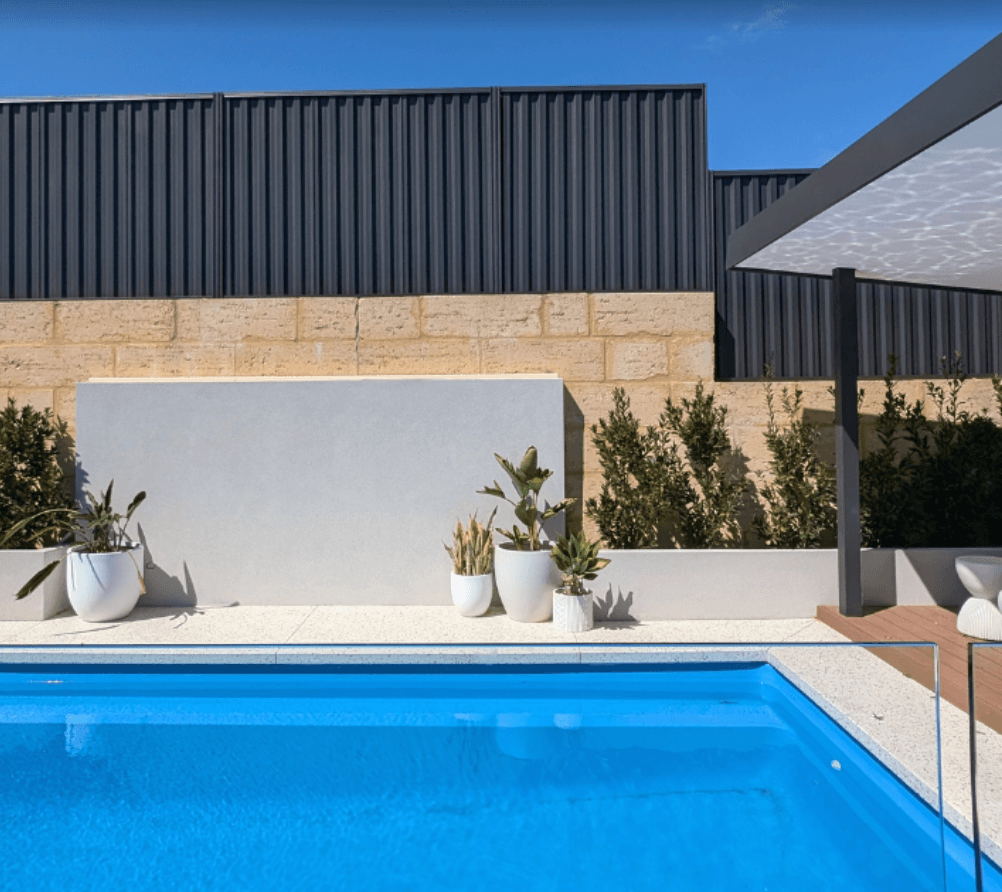 Charcoal Colorbond boundary fence above a limestone feature wall and rendered planter boxes in a Berwick pool area